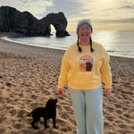 Person in yellow sweatshirt with a dog on a beach at sunset
