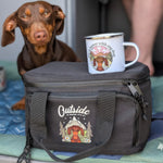 Dog with a cooler bag and mug featuring a dachshund design on a blue mat.