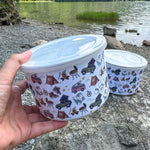 Two containers with lids, one held by a hand, against a scenic lake and mountains background.