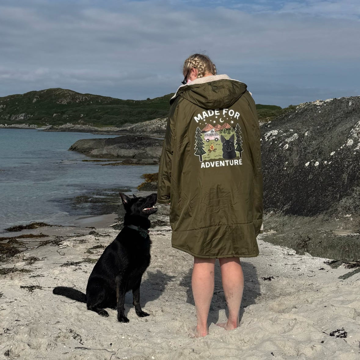 Person and black dog standing on a beach with a scenic background