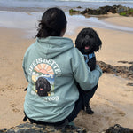 Person on a beach with a dog, wearing a hoodie with a graphic design.