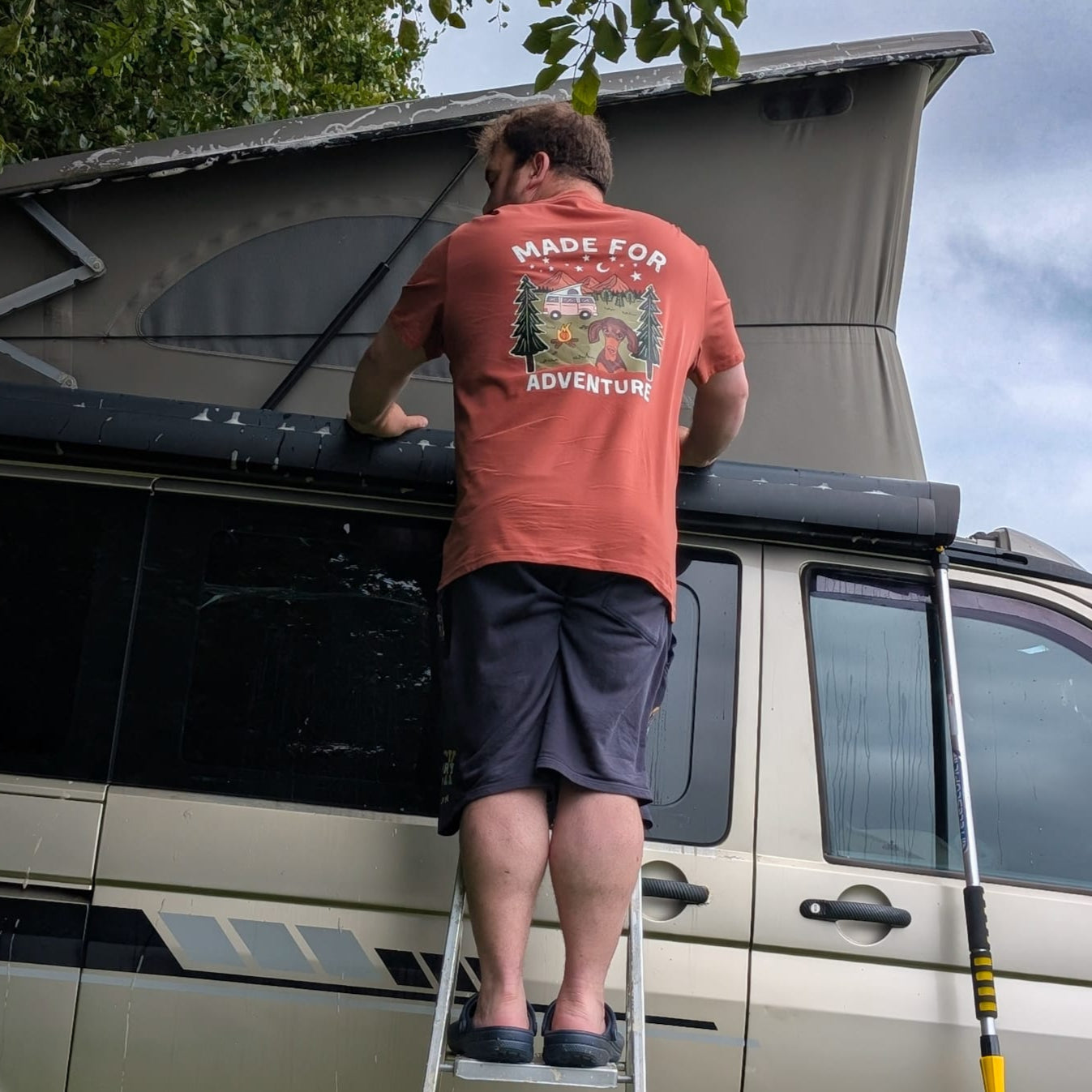 Person installing a roof rack on a van with a clear sky and trees in the background