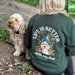 Person wearing a green sweatshirt with 'Life is better with my dog' text and a dog illustration, standing in a forest with a dog.