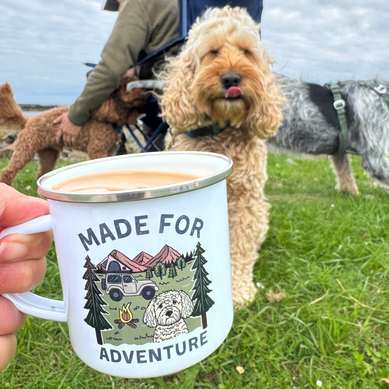 Person holding a 'Made for Adventure' mug with dogs in the background