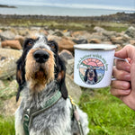 Dog sitting on a grassy area with a person holding a mug featuring a dog illustration.