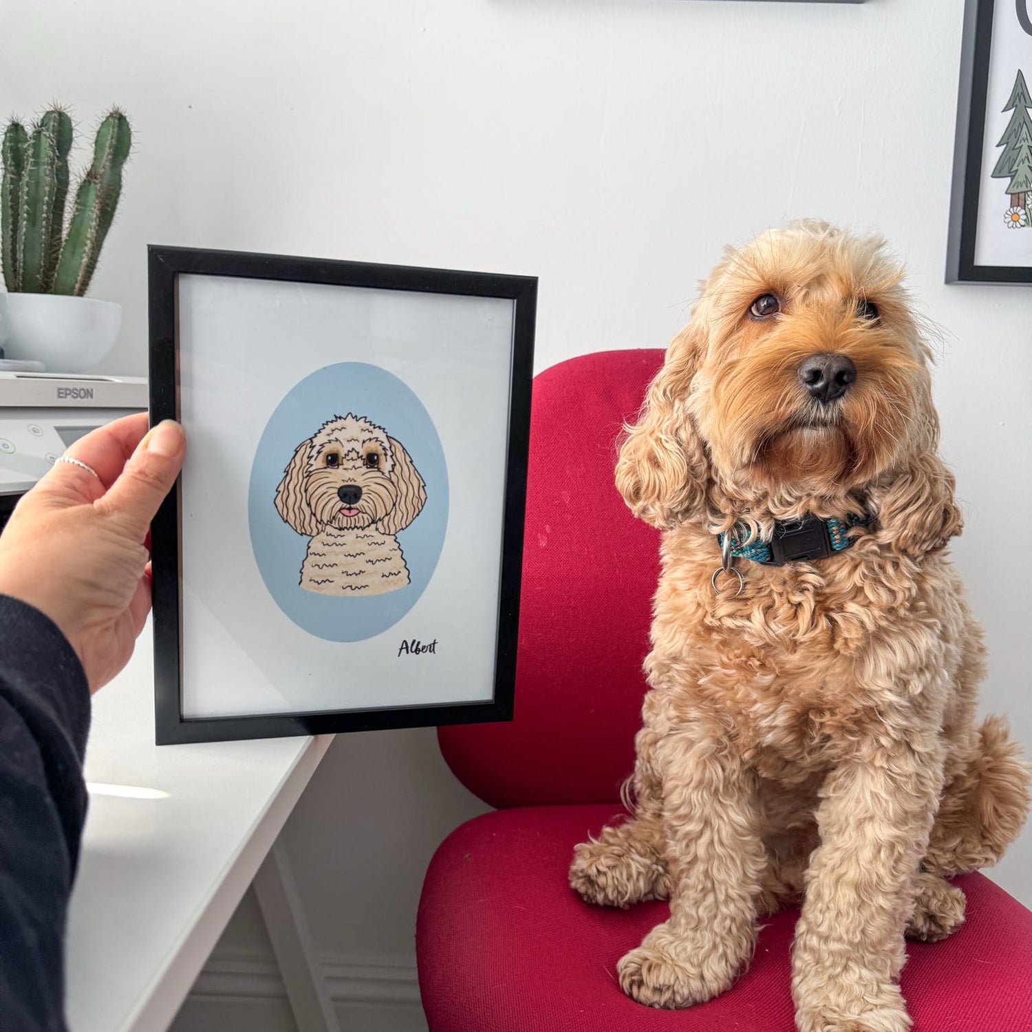 Dog sitting on a red chair next to a framed illustration of itself