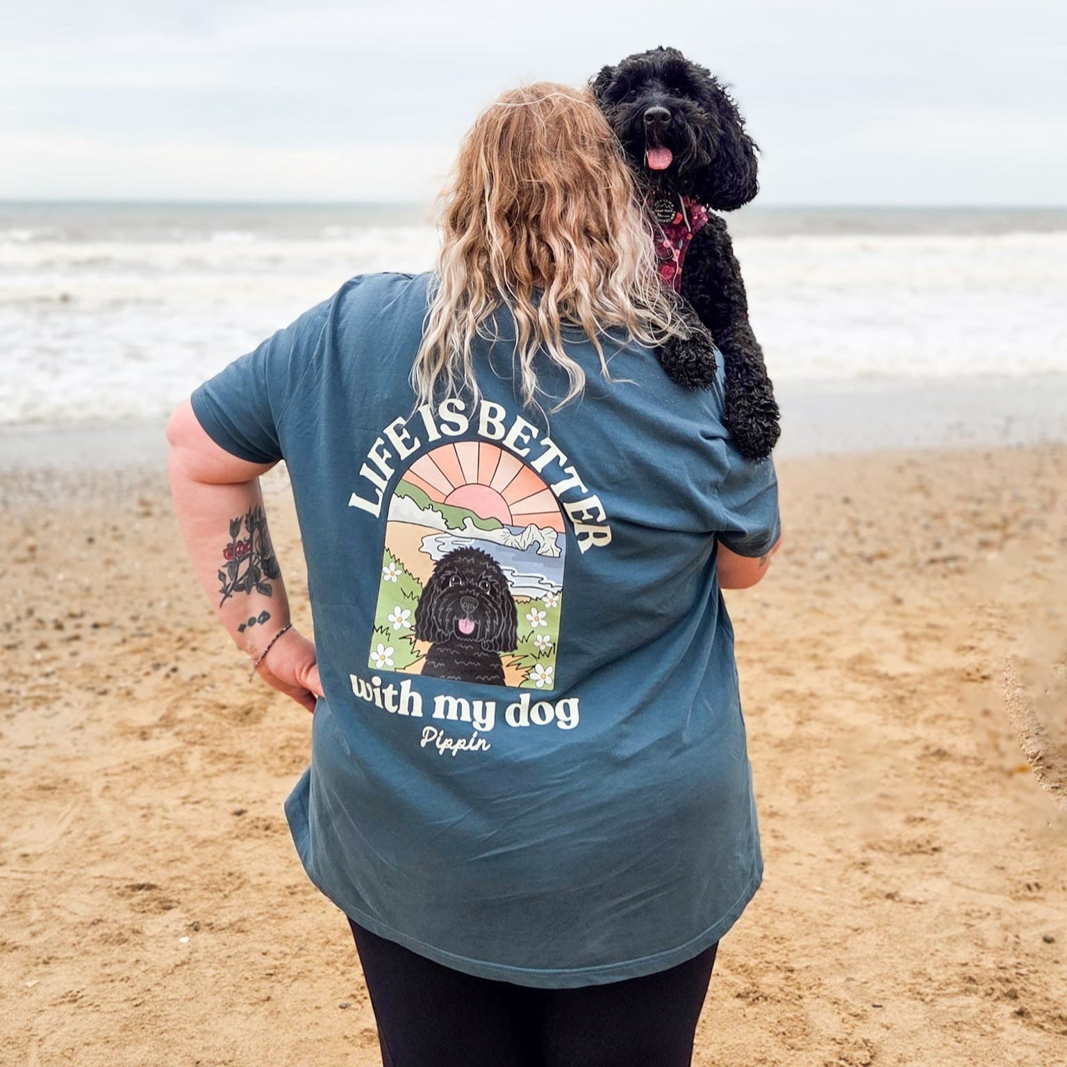 Person on a beach with a dog, wearing a t-shirt with a graphic and text.