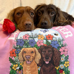 Two dogs with a shirt featuring their portraits and floral design, with a rose on a pink background.