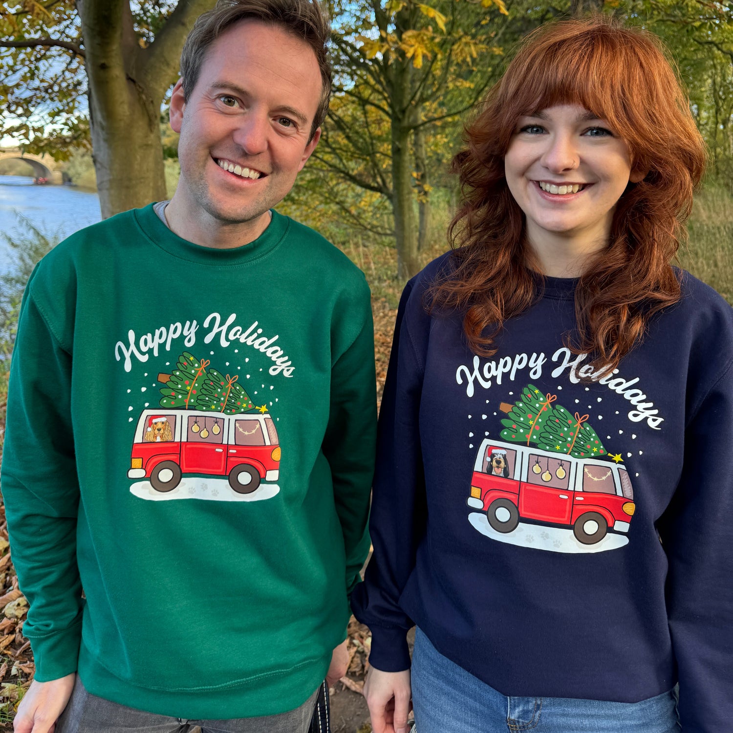 Two people wearing festive sweatshirts with a tree and car design outdoors.