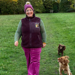 Person walking two dogs in a grassy field with trees in the background