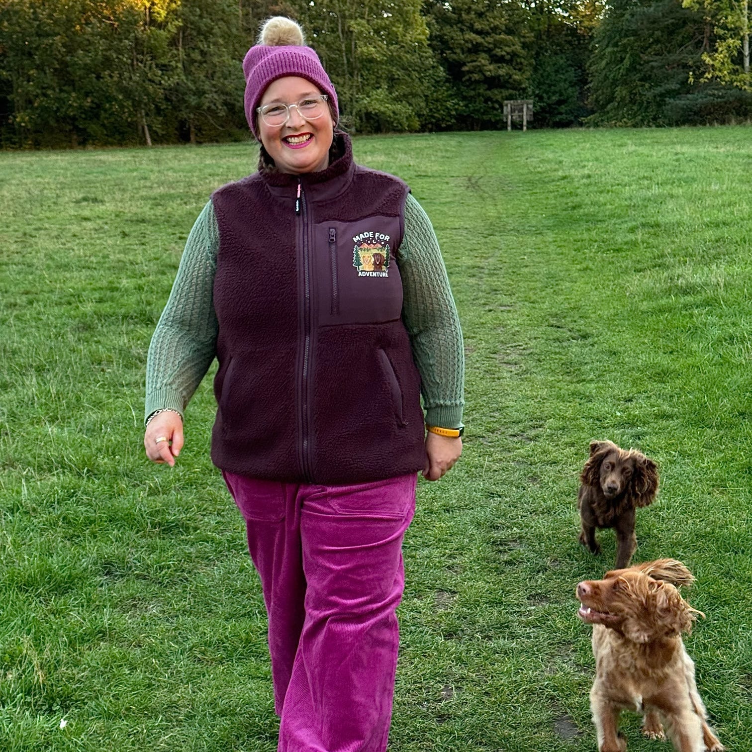 Person walking two dogs in a grassy field with trees in the background