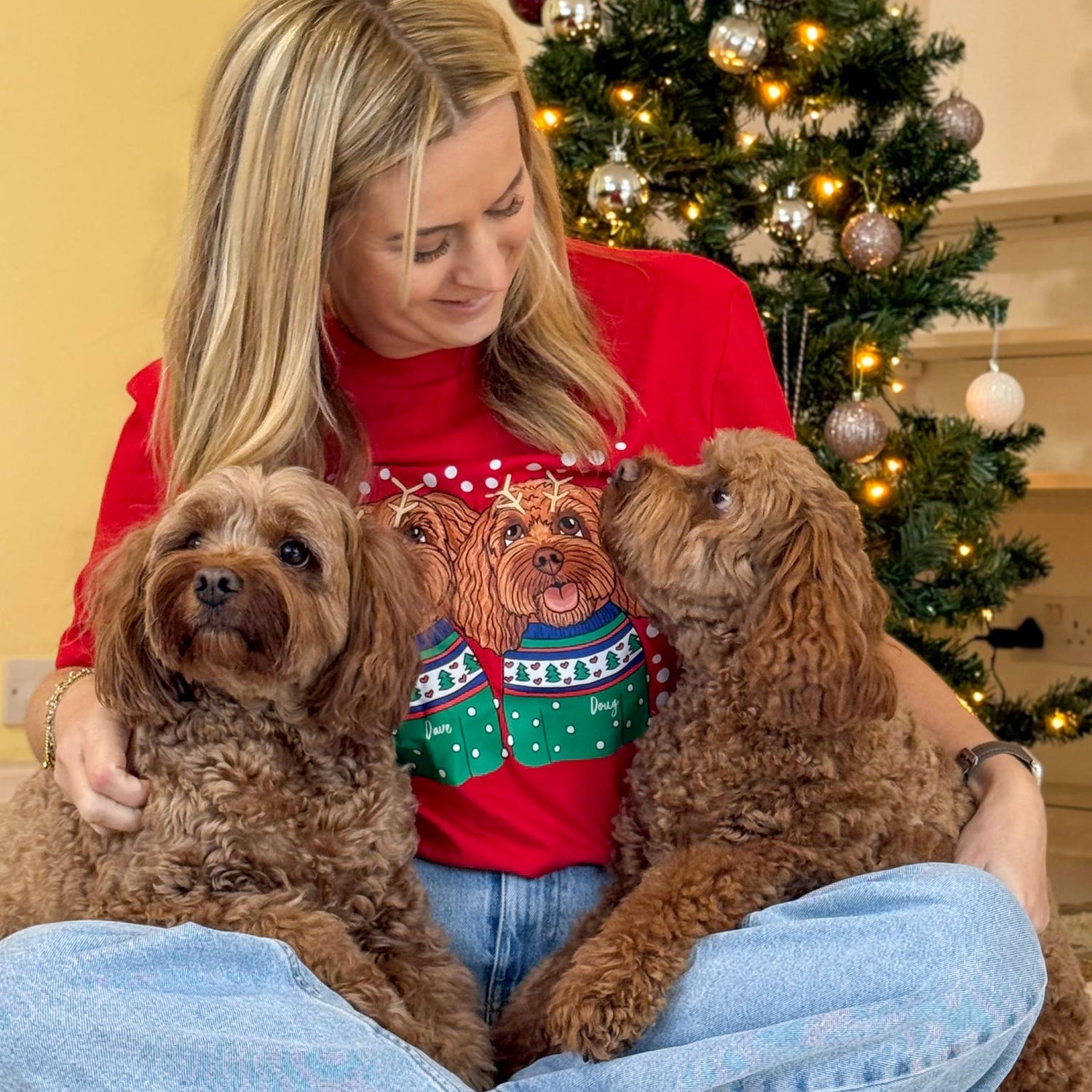 Woman in a red sweater with three dogs in front of a decorated Christmas tree.