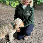 Woman in a green jacket with a logo petting a dog in a forest