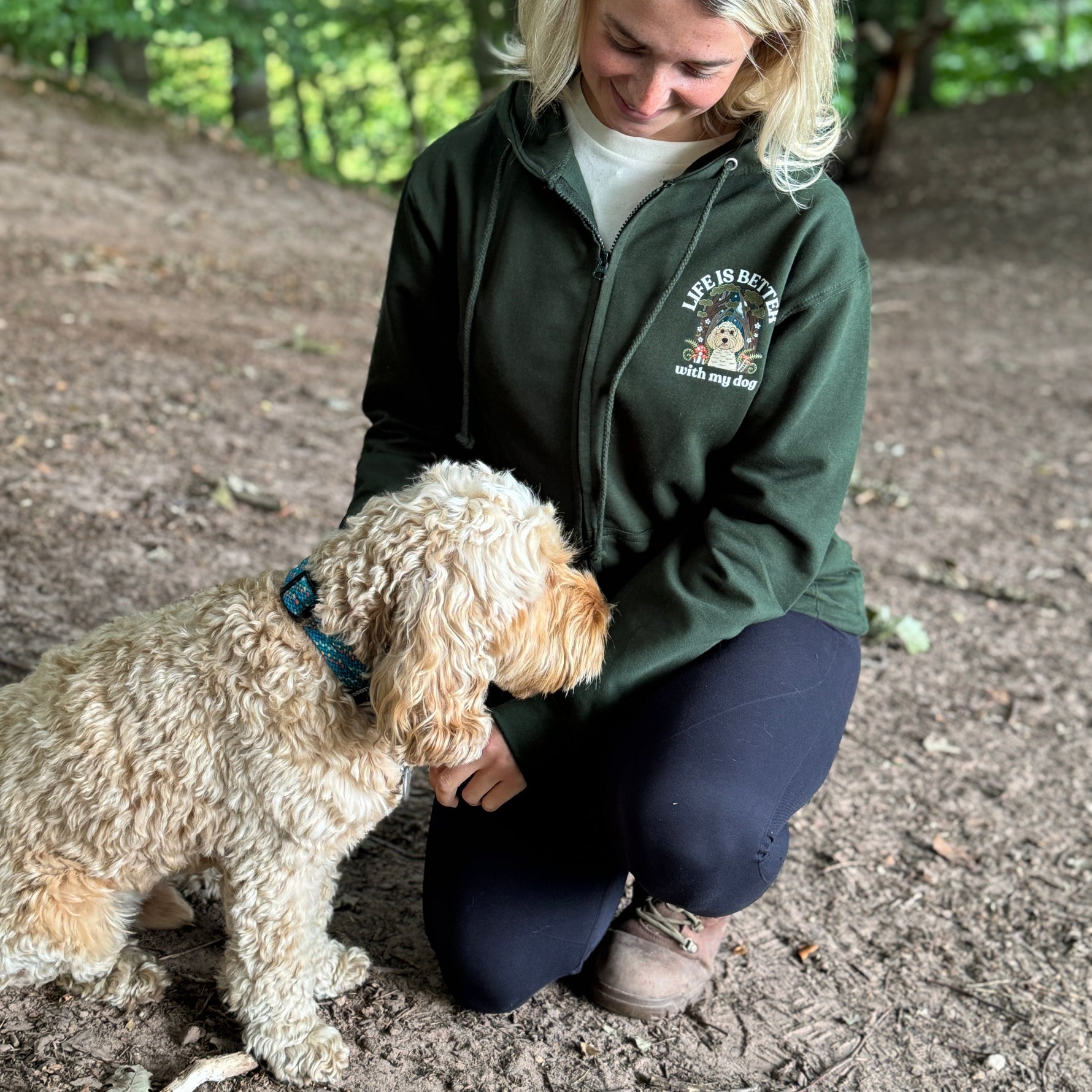 Woman in a green jacket with a logo petting a dog in a forest