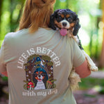 Person wearing a t-shirt with a dog graphic and 'Life is better with my dog' text, holding a dog in a forest.
