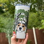 Tumbler with a dog illustration held in front of a green outdoor background