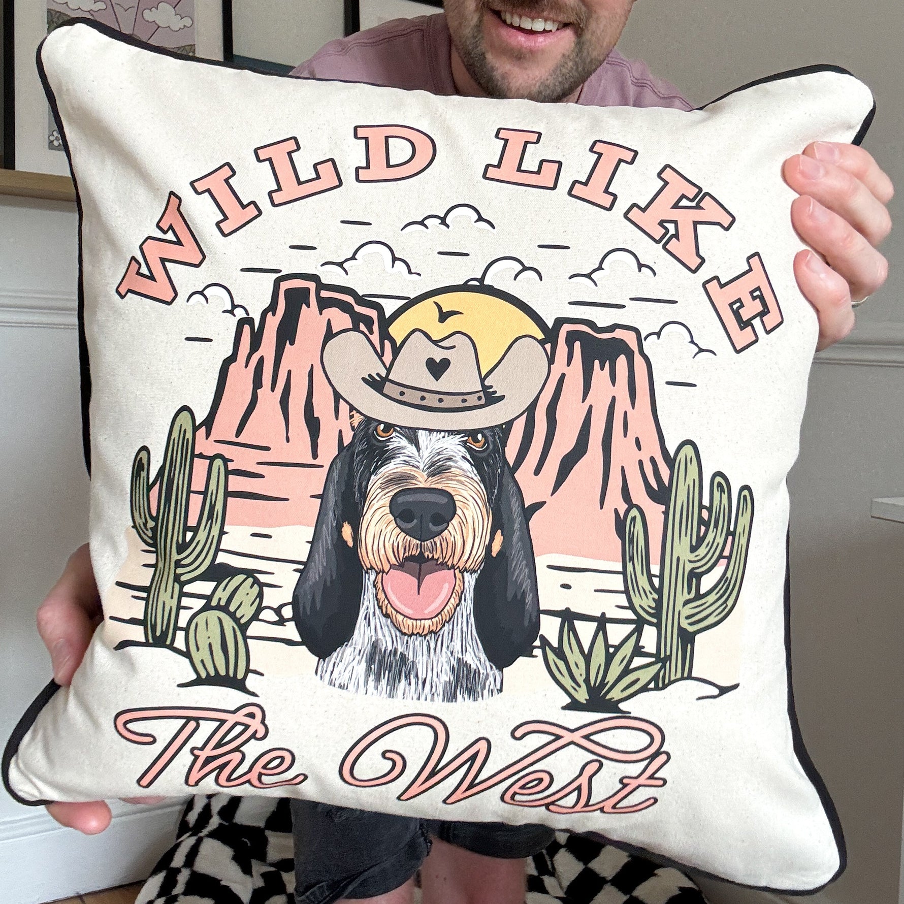 Person holding a pillow with a dog illustration and 'Wild Like the West' text.