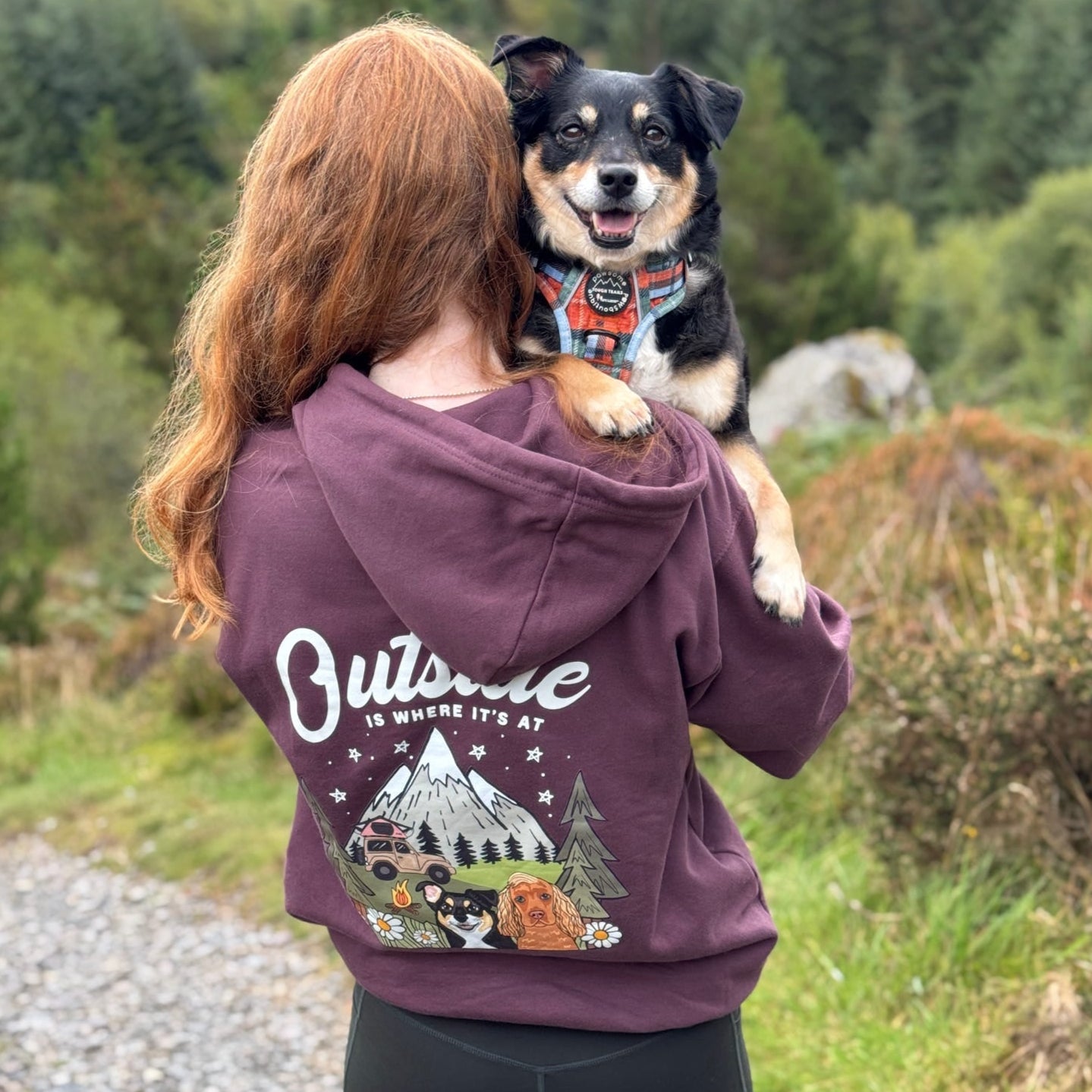 Person wearing a hoodie with a dog on their shoulders in a forest setting