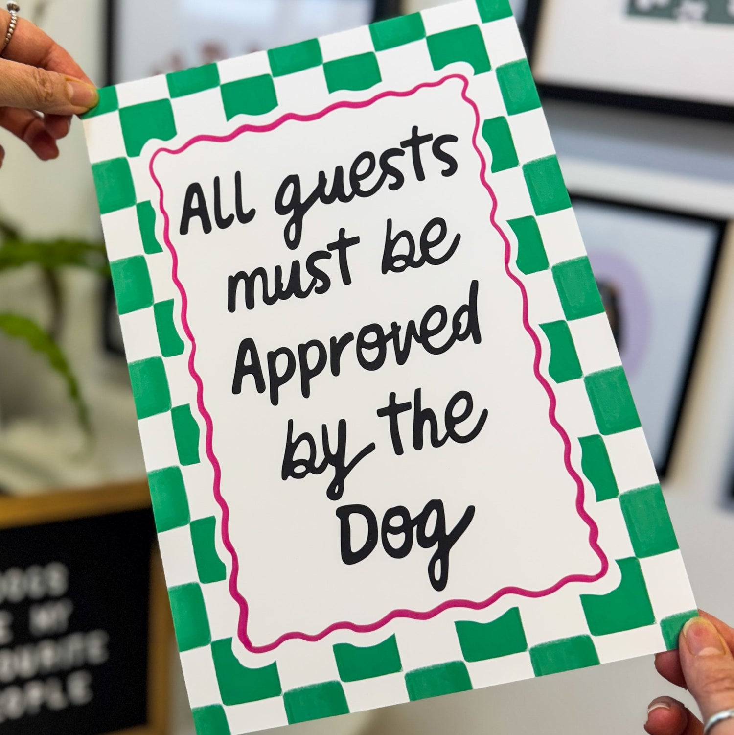 Checkered sign with text 'All guests must be approved by the dog' held by a person.
