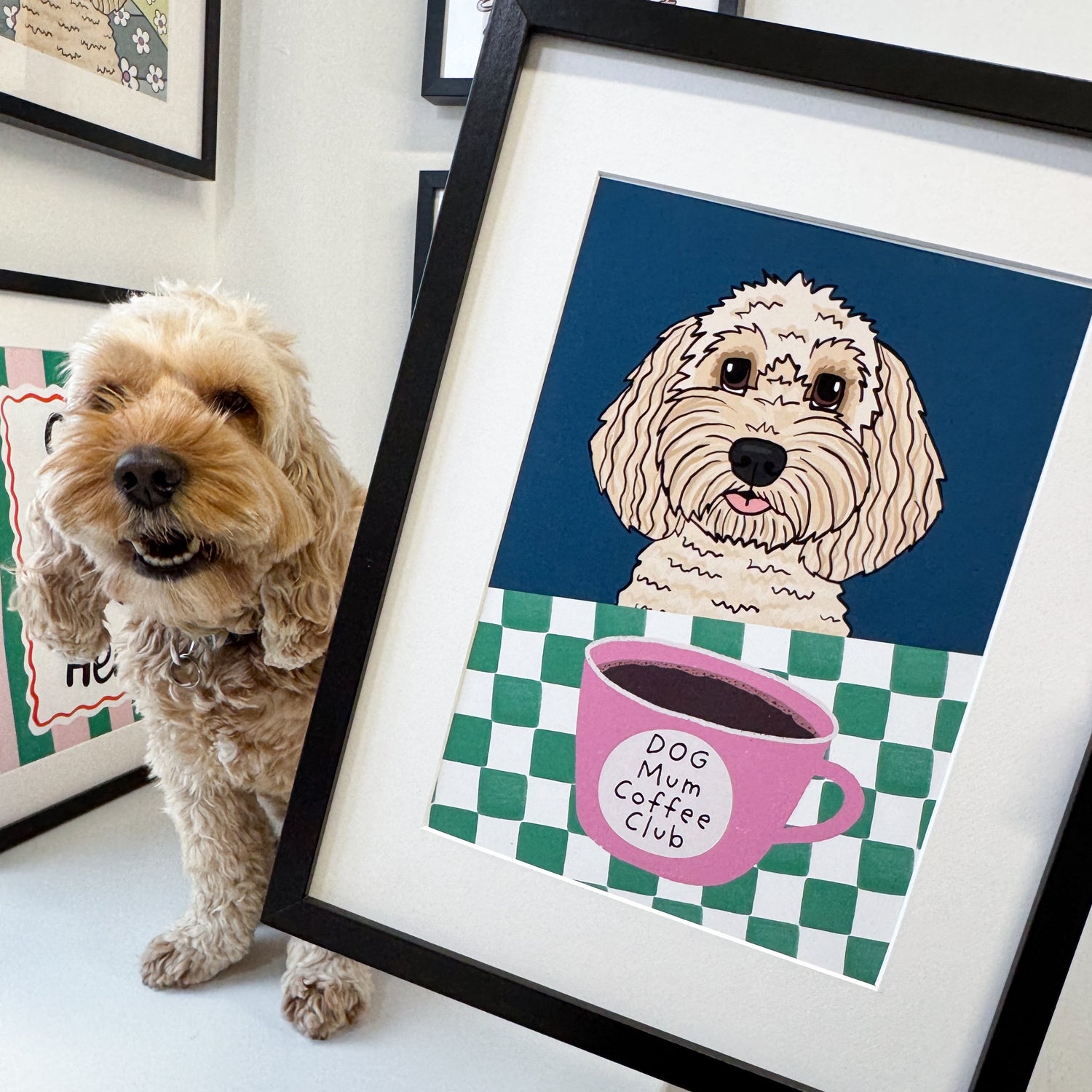 Dog standing next to a framed illustration of a dog with a coffee cup on a checkered background.
