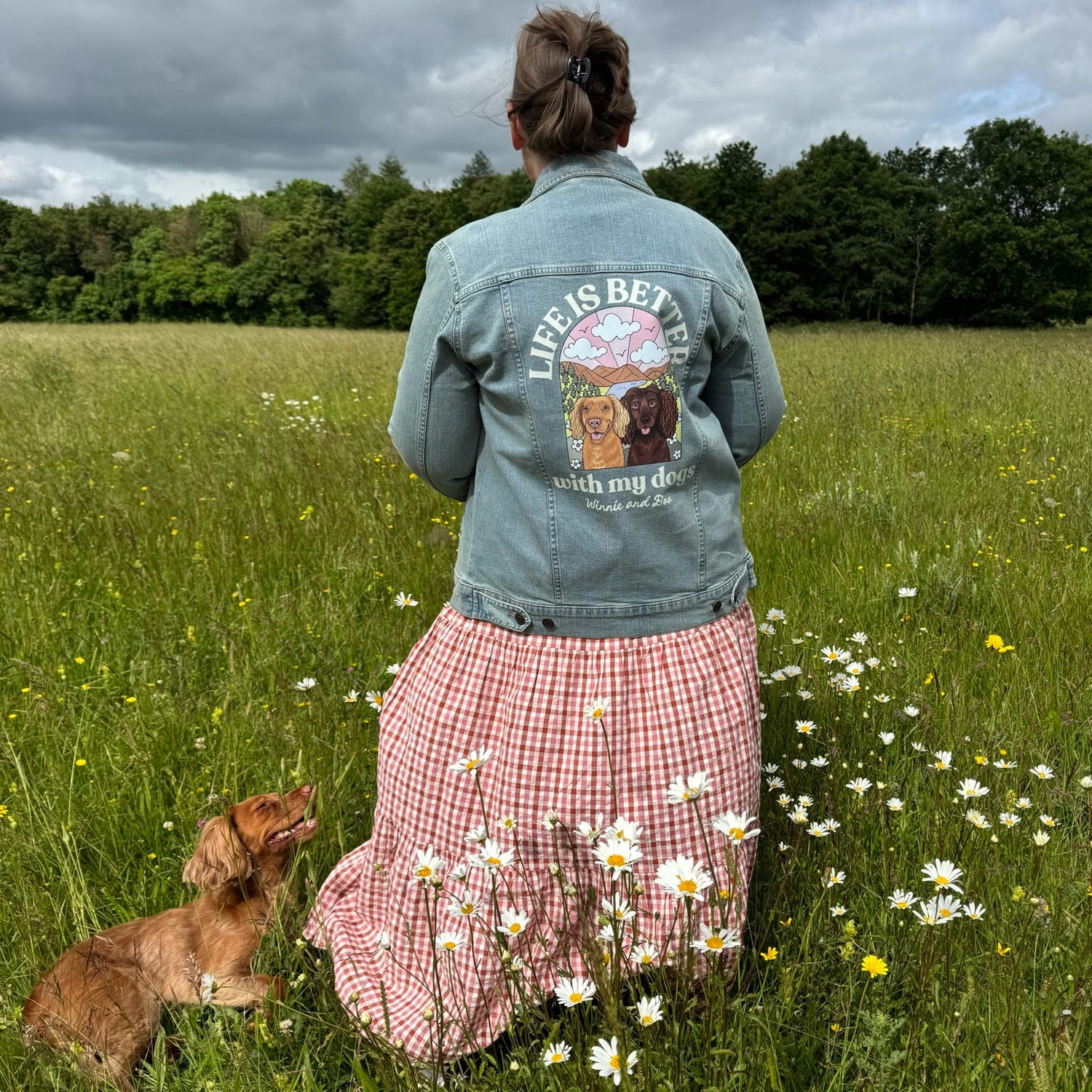 Person wearing a 'Life is Better with my Dog' jacket standing in a field with a dog.
