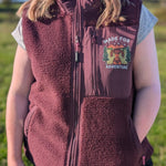 Person wearing a maroon fleece vest with a graphic design in an outdoor setting