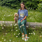 Woman sitting on a log with a dog in a field of flowers and trees