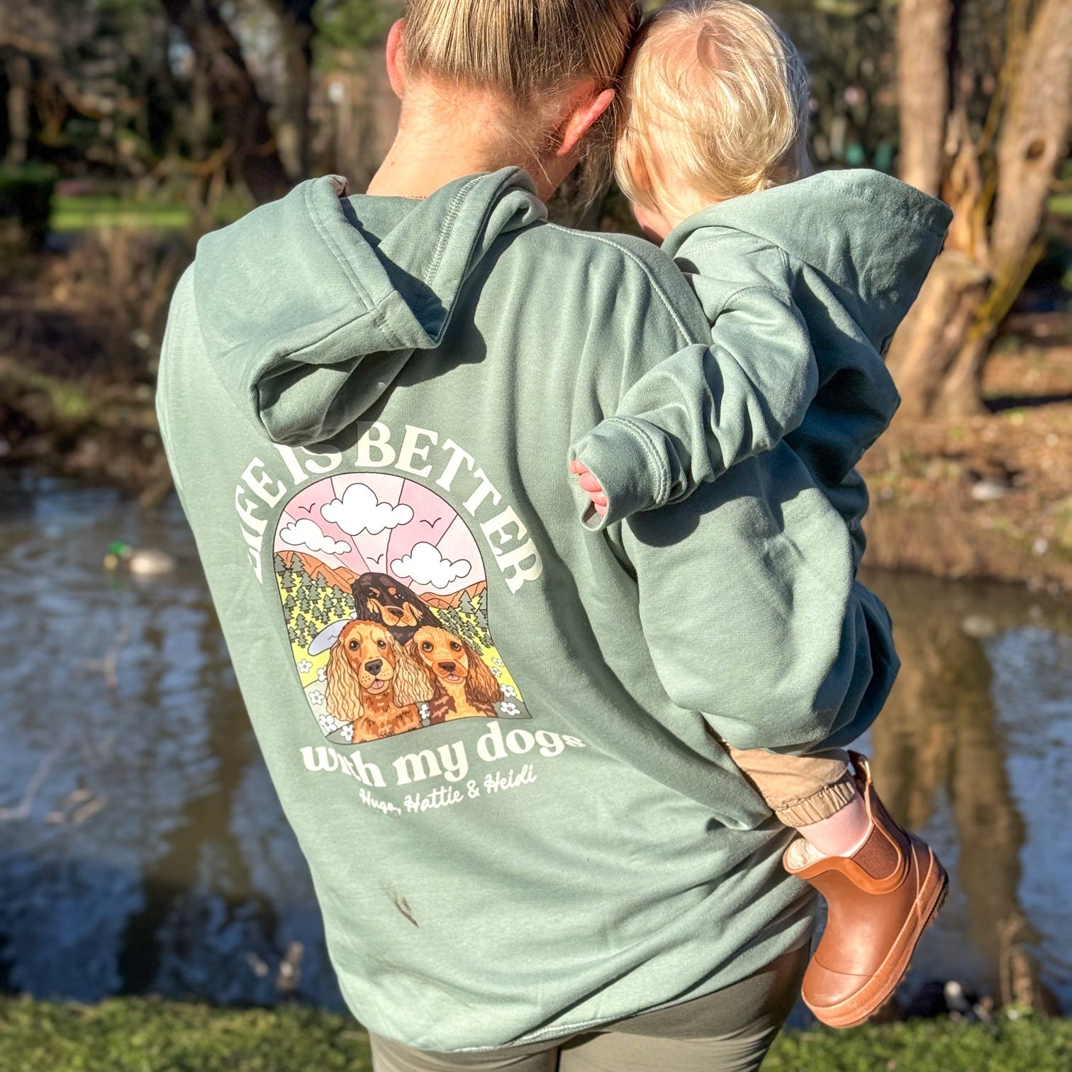 Woman and child wearing matching green hoodies with a dog-themed design in a park setting.
