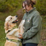 Woman in a green jacket holding a golden retriever in a forest setting