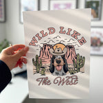 Person holding a tote bag with a dog graphic and 'Wild Like The West' text.