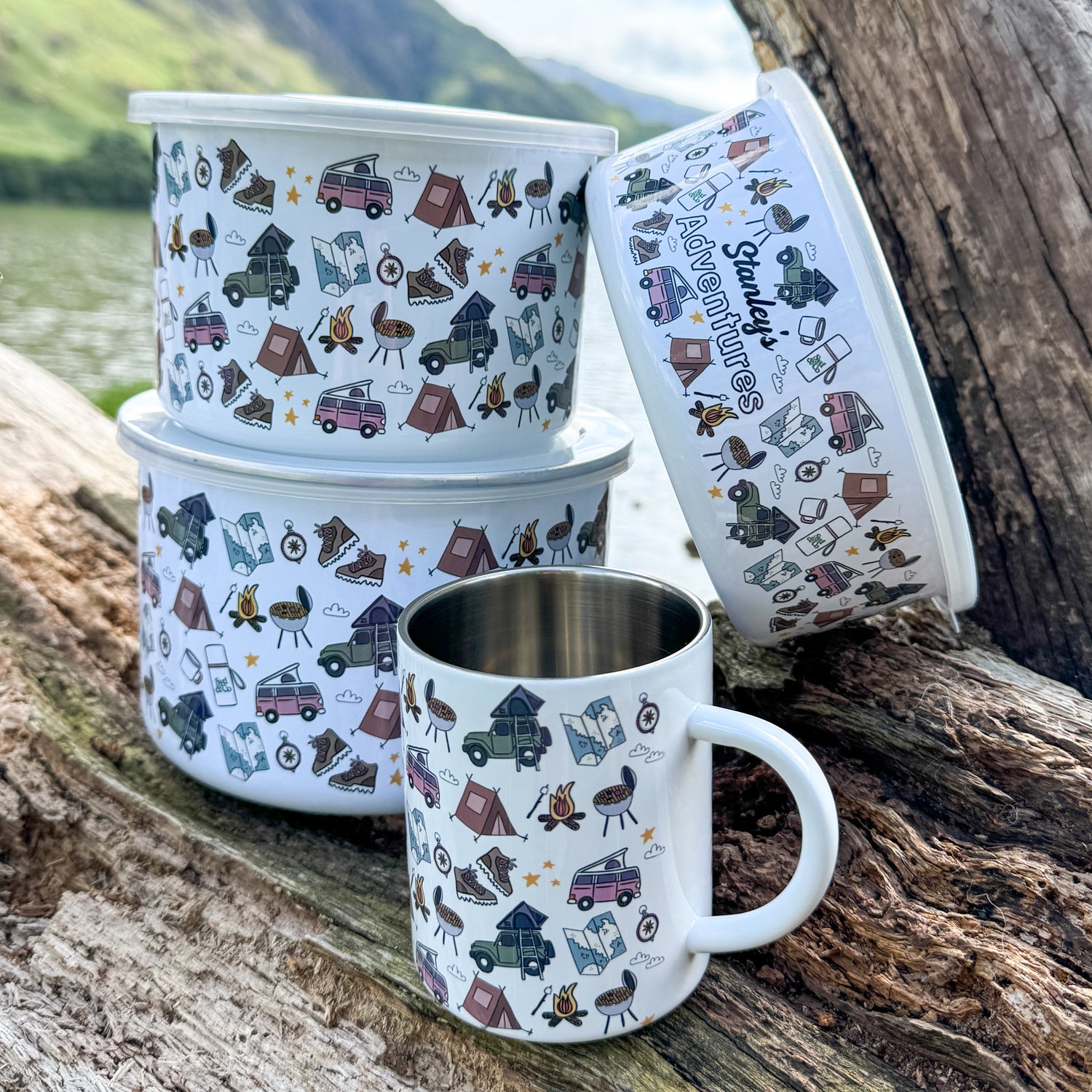 Set of camping-themed mugs and containers on a wooden surface with a scenic background.