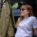 Woman wearing a white t-shirt with graphics and text, sitting next to a green jacket inside a vehicle.