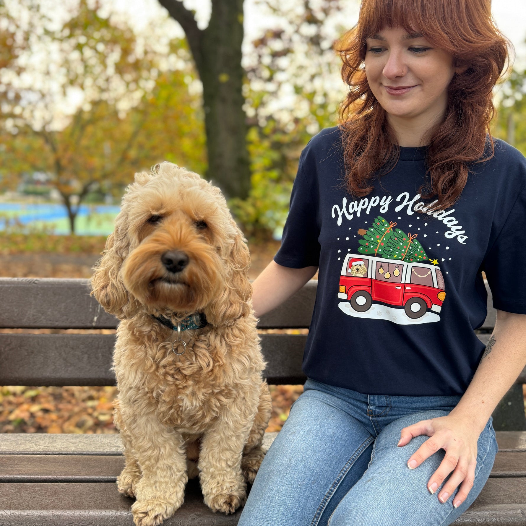 Woman wearing a 'Happy Holidays' t-shirt with a dog on a bench outdoors.