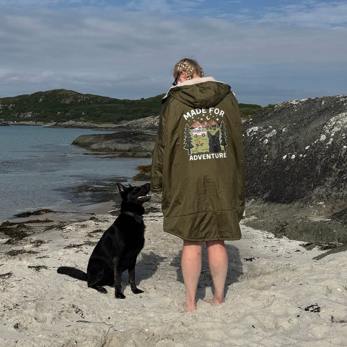 Person wearing a green jacket with a dog on a beach