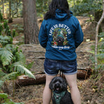 Person wearing a blue hoodie with 'Life is better with my dog' text in a forest setting.