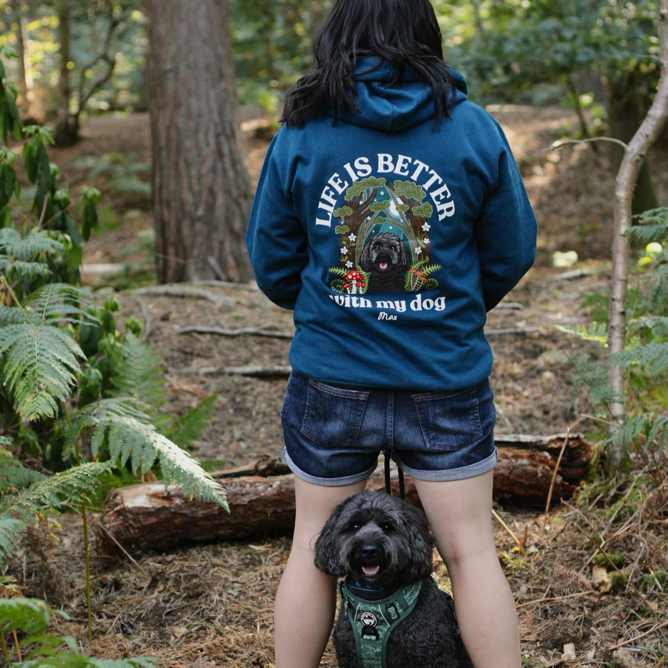 Person wearing a blue hoodie with 'Life is better with my dog' text in a forest setting.