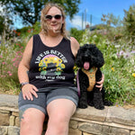 A woman sitting outdoors on a stone wall with her black poodle dog. She is wearing a black graphic vest top that reads 'LIFE IS BETTER with my dog' with a sunflower and dog illustration.