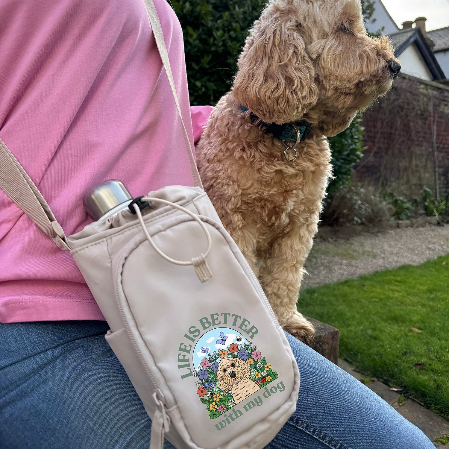 Person with a beige crossbody bag featuring a dog illustration and text, accompanied by a dog outdoors.