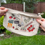 Beige pouch with gardening-themed illustrations held in front of a garden background