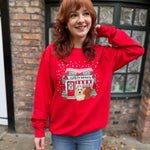 Woman wearing a red sweatshirt with a dog and bakery design, standing in front of a brick building.
