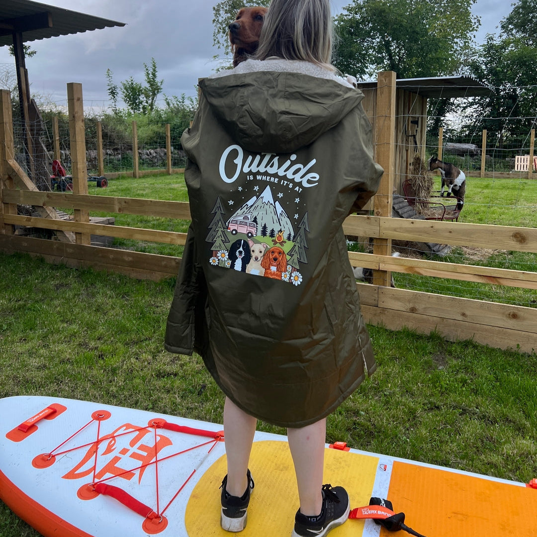 Person standing on a paddleboard wearing a green jacket with 'Outside' branding.