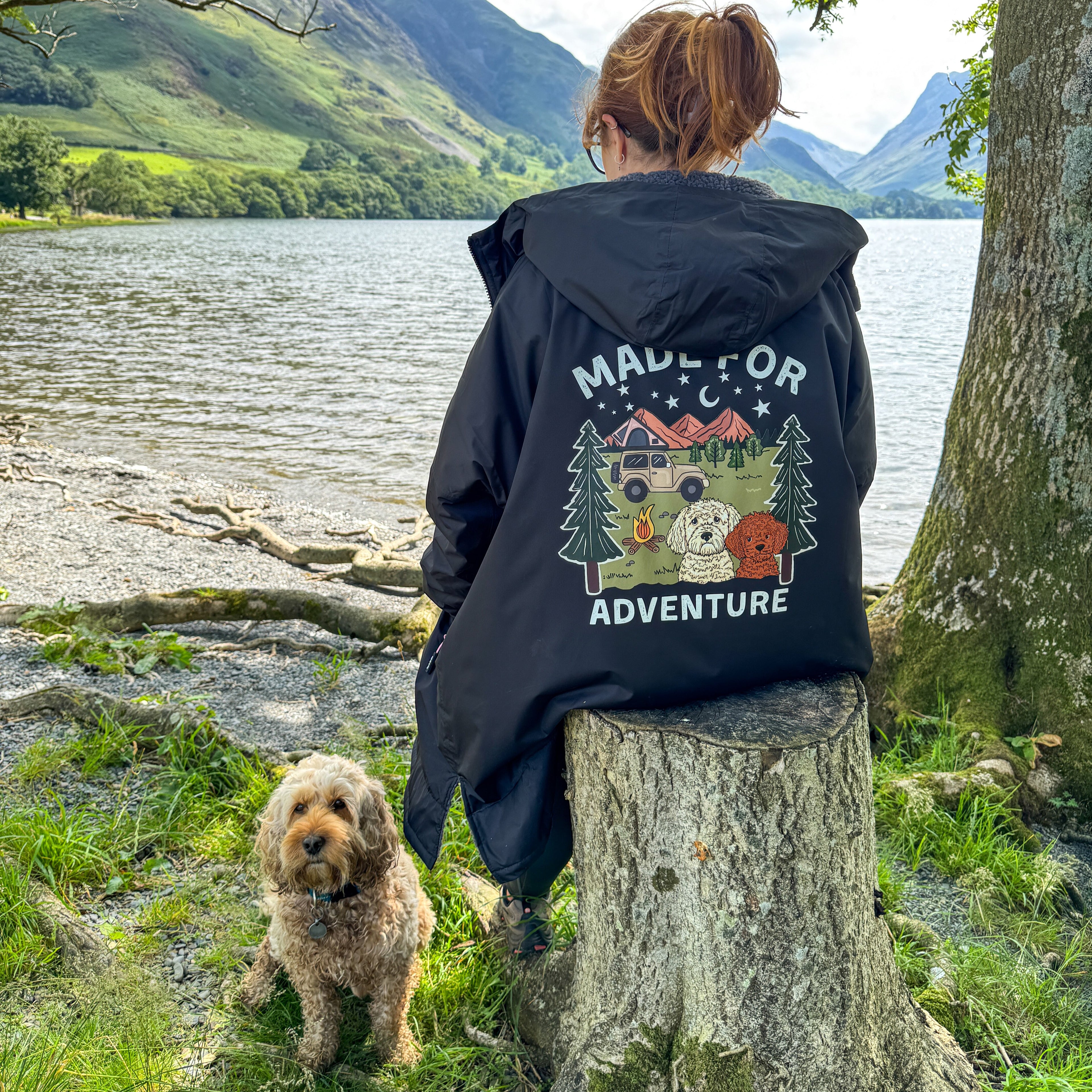 Person wearing a jacket with 'Made for Adventure' design by a lake and mountains