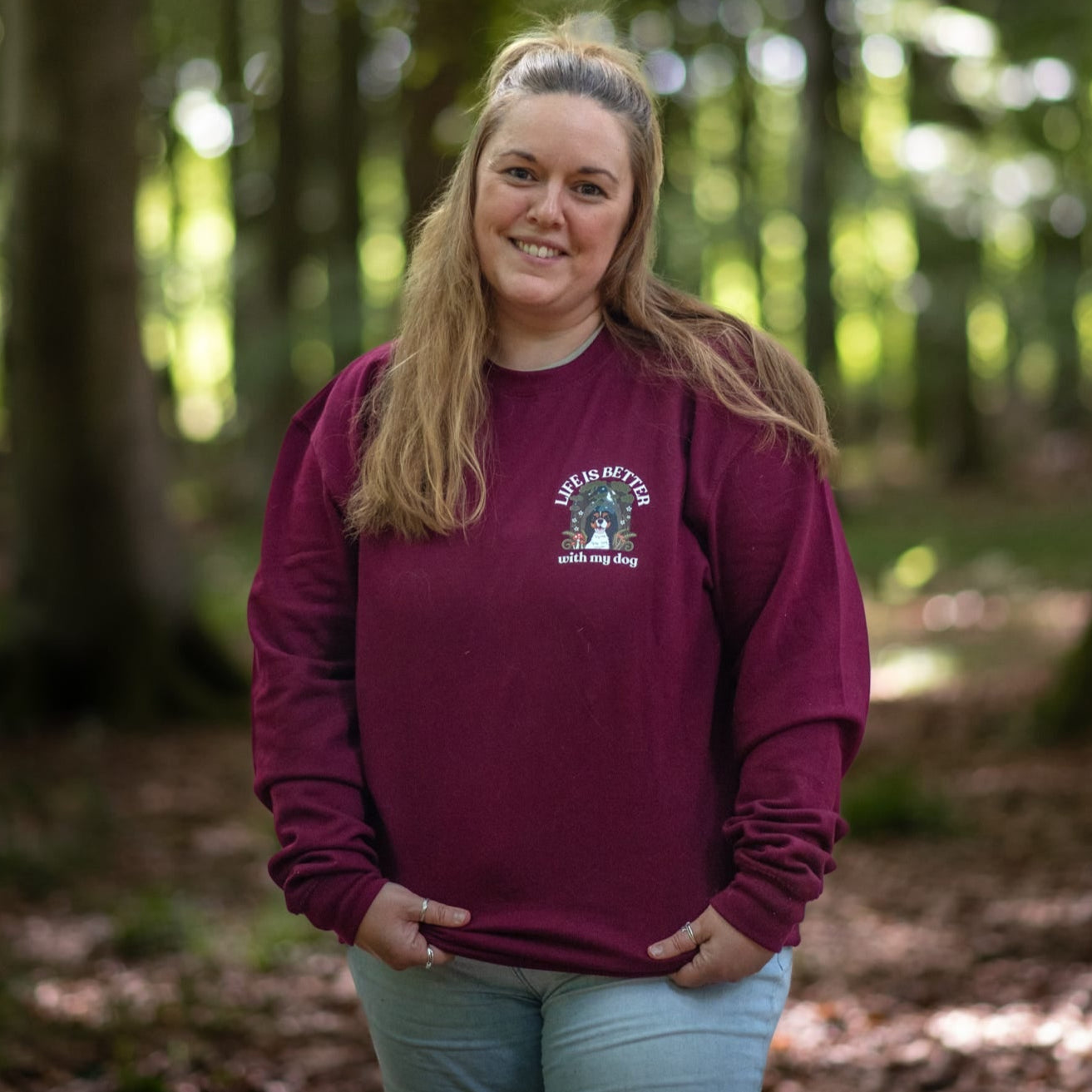 Woman wearing a maroon sweatshirt with a logo in a forest setting