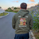 Person wearing a green hoodie with a graphic design and text, standing on a road with a scenic background.