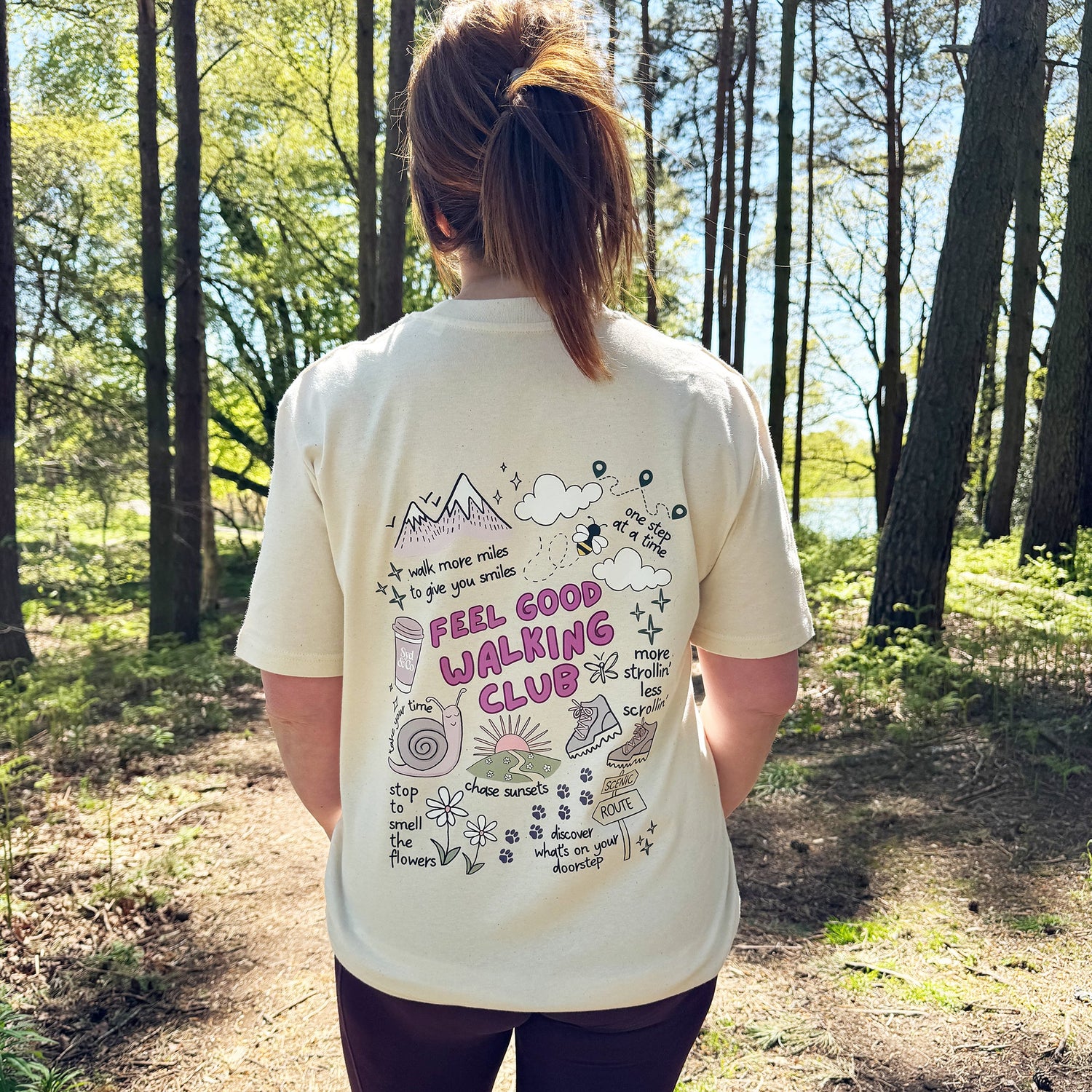 Person wearing a 'Feel Good Walking Club' t-shirt in a forest setting