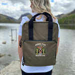 Person wearing a green backpack with 'Made for Adventure' text and dog illustration by a lake.