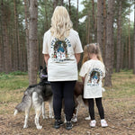 Two people and two dogs standing in a forest setting wearing matching t-shirts.