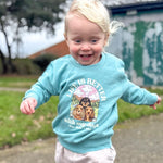 Child wearing a light blue sweatshirt with a dog-themed design outdoors.