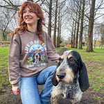 Person wearing a sweatshirt with a dog graphic and text, kneeling next to a dog in an outdoor setting.