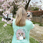 Woman wearing a teal t-shirt with a dog graphic and 'Life is better with my dog' text, standing in a park with cherry blossoms.